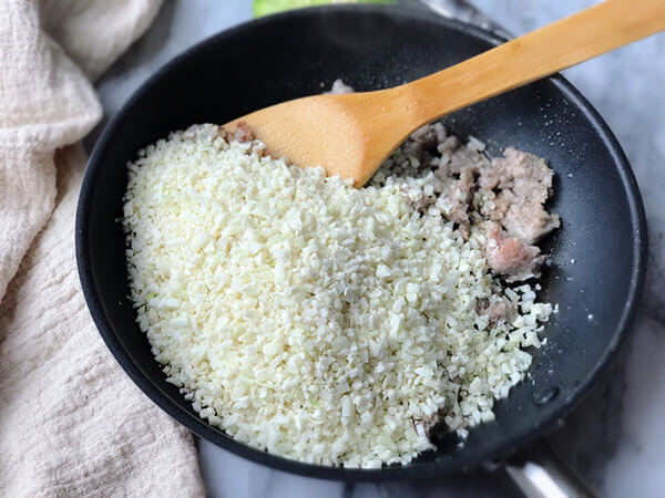 Adding the cauliflower rice to the pan.